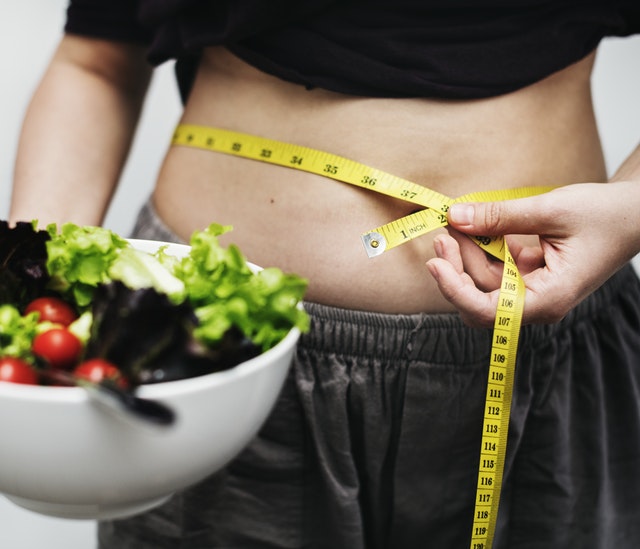 woman measuring her waistline and holding a salad
